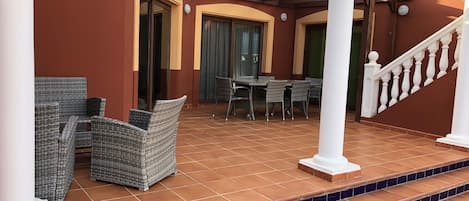 A covered outdoor area with wicker furniture, a tiled floor, and a staircase leading to a higher level.