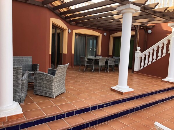 A covered outdoor area with wicker furniture, a tiled floor, and a staircase leading to a higher level.