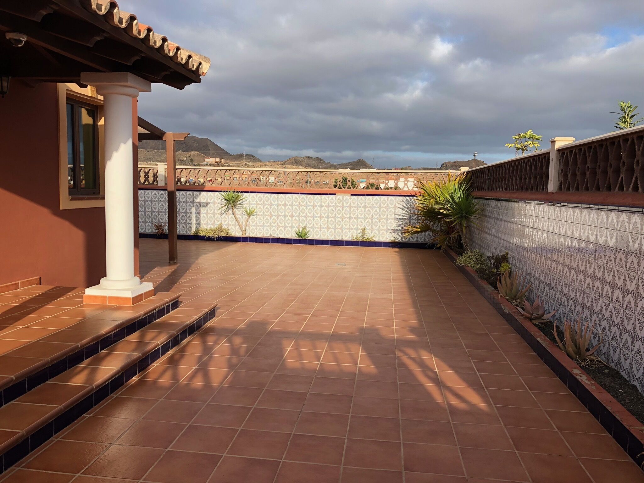 Eine Terrasse mit Terrakottafliesen, einer weißen Säule und einer Wand mit Muster.