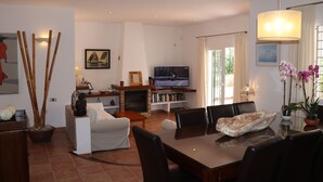 Un salon comprenant un téléviseur, un canapé, une table à manger, des chaises et une cheminée.