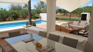Un espace aménagé au bord de la piscine, comprenant une table à manger, des chaises, un canapé et un téléviseur.