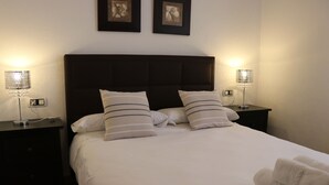 Un lit bien fait, avec du linge de lit blanc et des oreillers à rayures, flanqué de deux tables de chevet sur lesquelles sont posées des lampes.