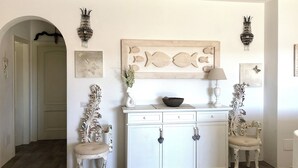 A room with a white cabinet, two decorative chairs, a vase with flowers, and wall art including fish and bird designs. - House 50 meters from the sea residence S'ABBA E SA PEDRA  (Golfo Aranci)