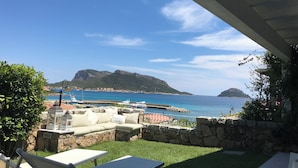 A patio with outdoor seating, a stone wall, and a view of the sea and mountains. - House 50 meters from the sea residence S'ABBA E SA PEDRA  (Golfo Aranci)