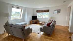 A spacious living room with a wooden floor, two grey sofas, a small round table, and a TV on a wooden stand. - Unique property, in a peaceful and serene location,  within easy reach of all amenities. (Humbie)