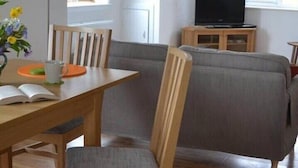 A room with a wooden dining table, chairs, a grey sofa, a TV on a wooden stand, and a window with a plaid curtain. - Unique property, in a peaceful and serene location,  within easy reach of all amenities. (Humbie)