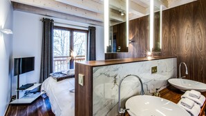 Een moderne hotelkamer met een groot bed, een televisie, een bureau met een laptop, een badkamer met een marmeren wastafel en een grote spiegel.