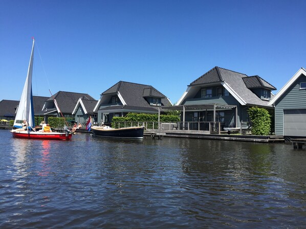 A canal with a sailboat docked near houses with sloped roofs and a covered area.