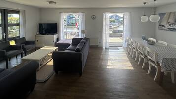 A living room with a sofa, a coffee table, and a TV. There is a dining area with a table and chairs.