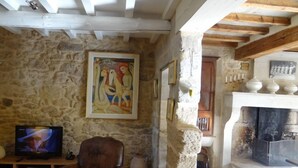 Un salon rustique avec des murs en pierre, un plafond en bois, une cheminée et un téléviseur.