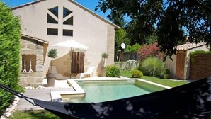 Un espace piscine agrémenté d’un hamac, un bâtiment en pierre et un jardin bien entretenu.