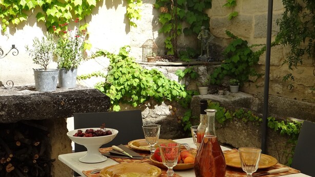 Un espace extérieur aménagé pour les repas, avec une table en pierre, des plantes en pot et une statue.