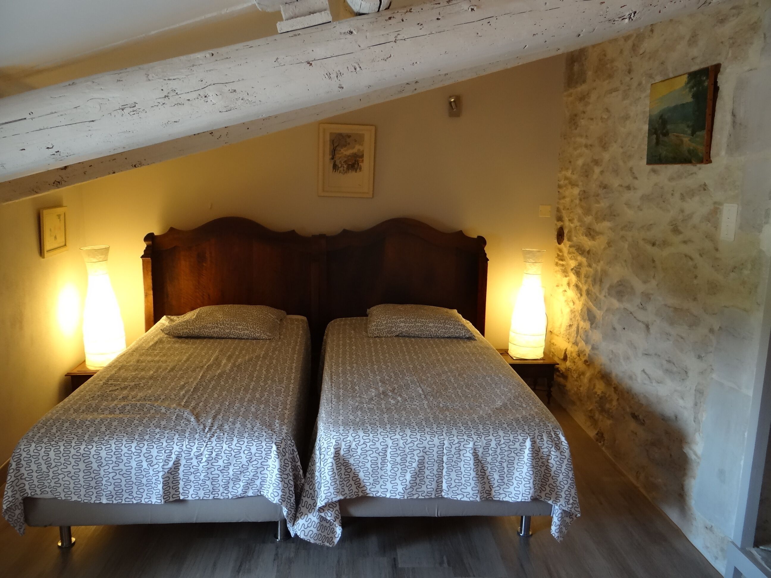 Ein Zimmer mit zwei Einzelbetten, Holz-Kopfteilen und zwei Nachttischlampen.