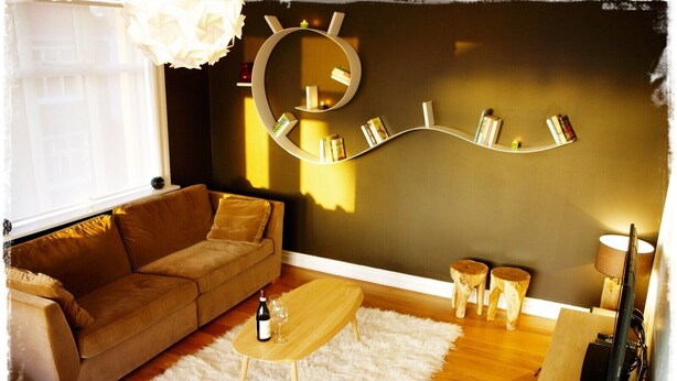 A cozy living room with a brown sofa, a wooden coffee table, a white furry rug, and a wall-mounted bookshelf with books and candles. - Exceptional Luxury Apartment In 101 Reykjavik, The Centre Of Town
 (Reykjavik)