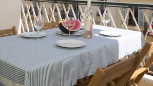 Une table placée sur un balcon, avec une bouteille, des verres et des assiettes, d’où l’on peut admirer un immeuble doté de balcons et de fenêtres.