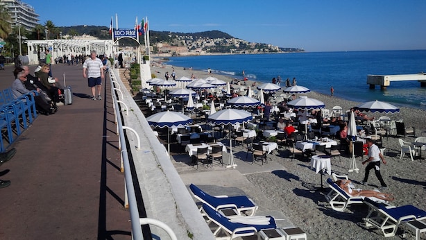 Un café situé en bord de mer, avec une terrasse et des parasols, offrant une vue sur l’océan.
