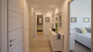 Une chambre d’hôtel moderne, équipée d’un lit, d’une coiffeuse avec un miroir et d’un couloir menant à la salle de bain.