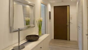 Un couloir moderne avec une coiffeuse blanche, un miroir et un vase contenant des fleurs blanches.