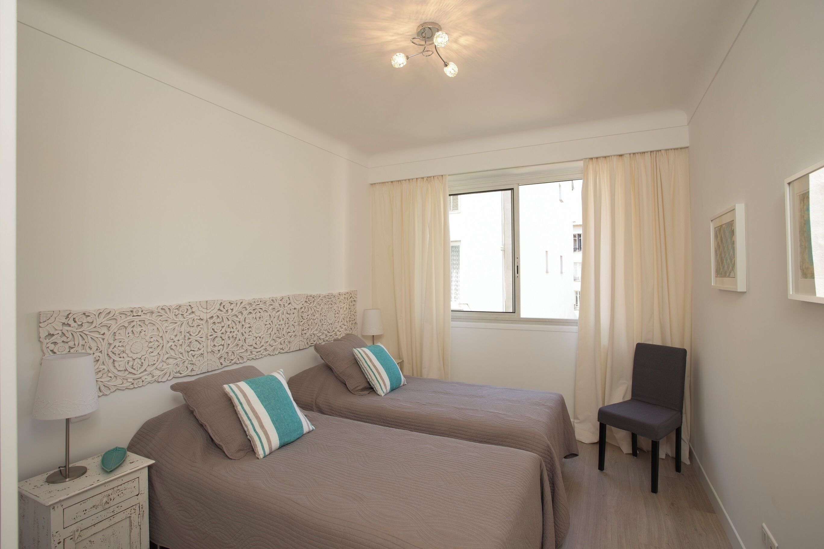 A bedroom with two beds, a chair, a nightstand, and a window with curtains.