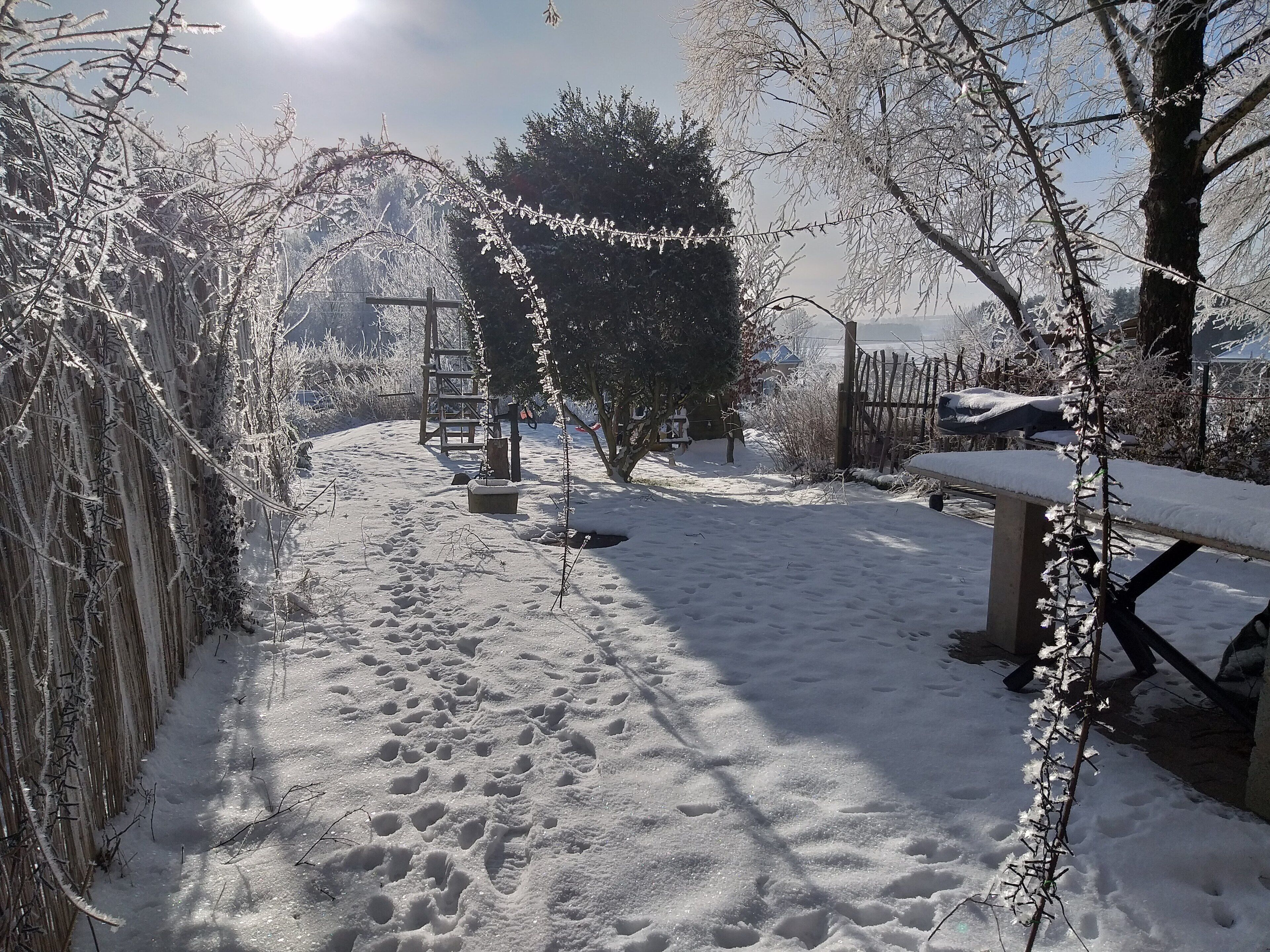 A snow-covered garden with a wooden bench, a ladder, and a metal table.