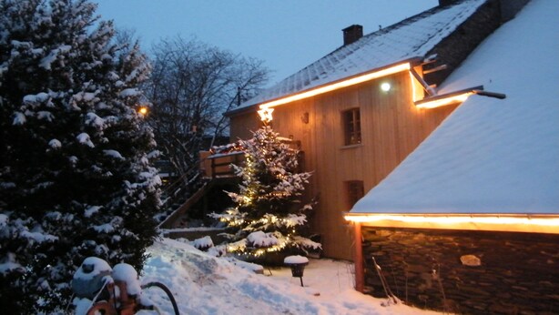 Una casa de madera con techo nevado y luces exteriores encendidas.