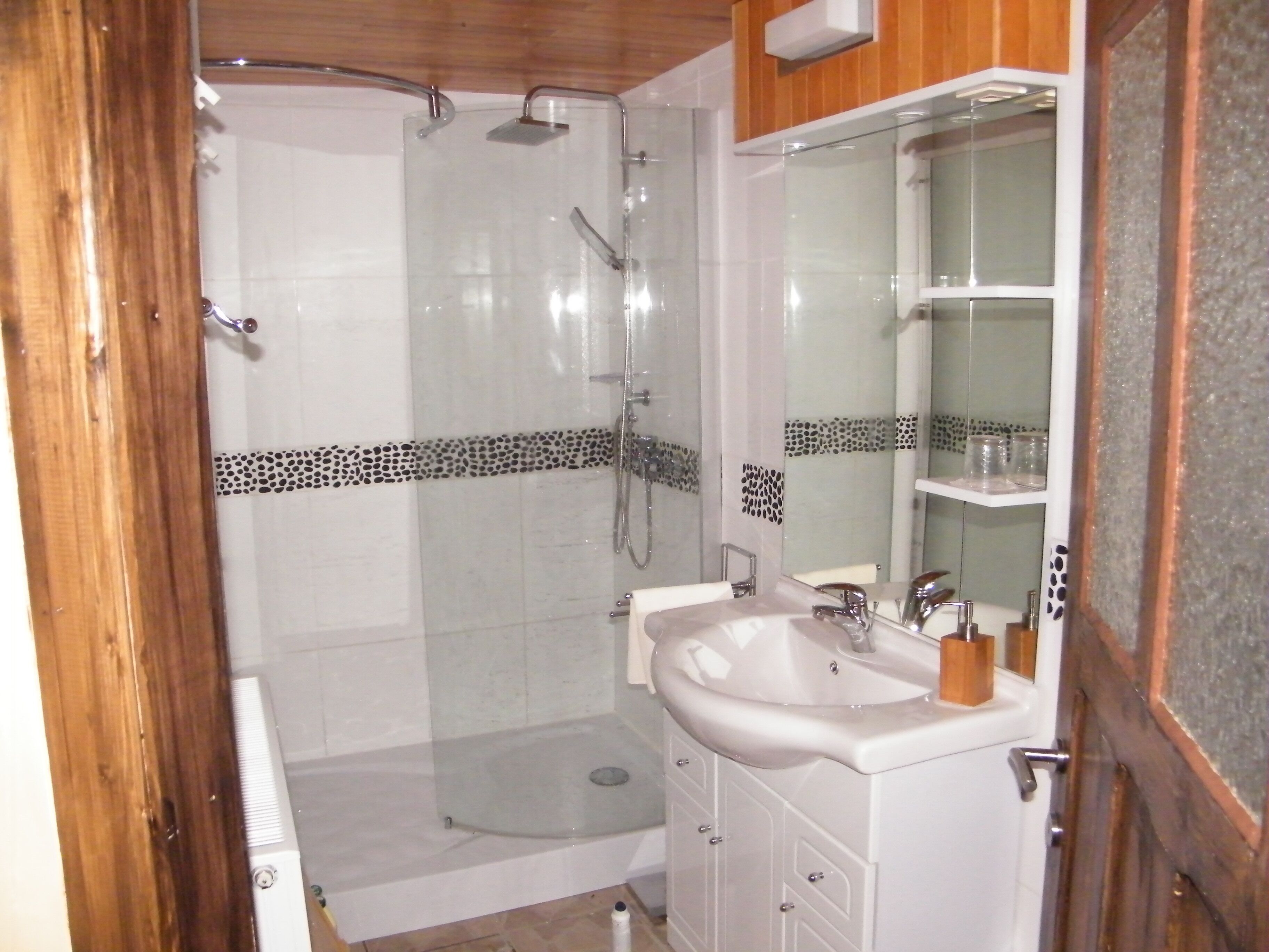 Une salle de bain avec une douche à parois de verre, un lavabo blanc avec un miroir et une porte en bois.
