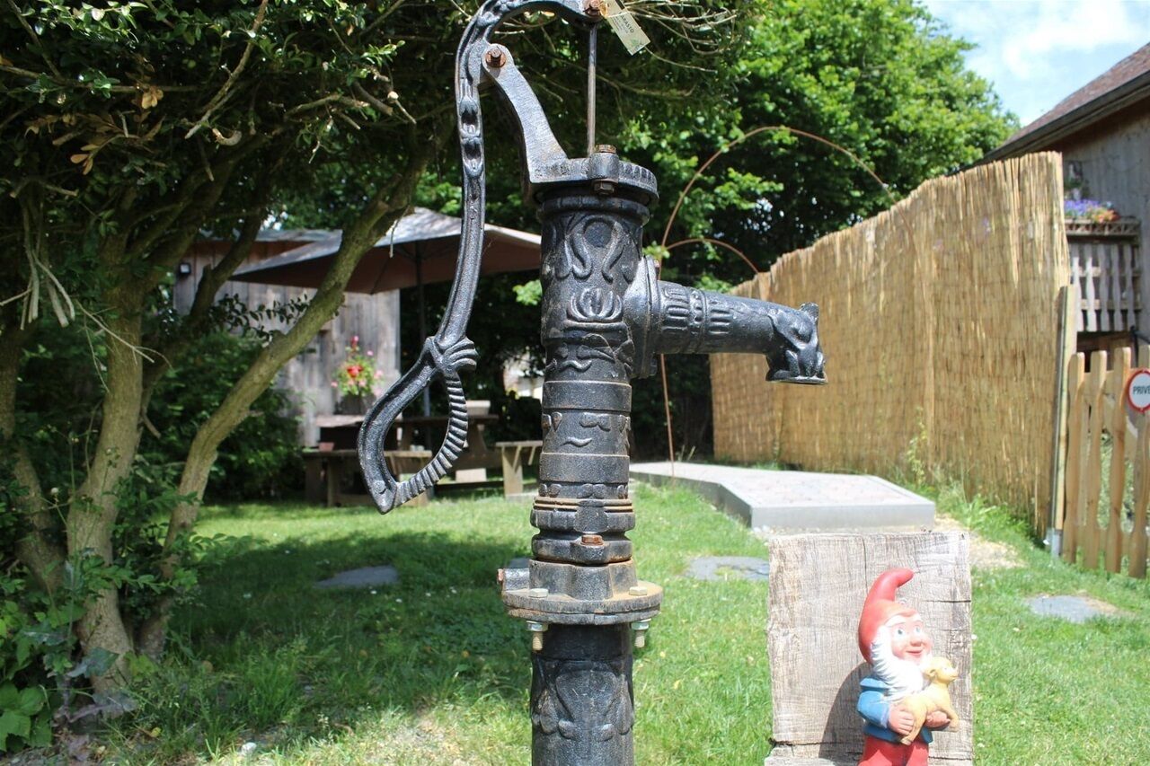 Eine ländliche Außenansicht mit einem verzierten Metall-Wasserhahn, einem Holzzaun und einer Gartenzwerg-Statue.