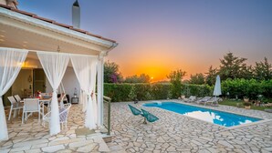 A stone patio with a swimming pool, outdoor seating, and a covered area with white curtains. - Villa With Private Pool (Magganos)