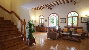Un salón espacioso con escalera de madera, chimenea y amplios ventanales de arco.