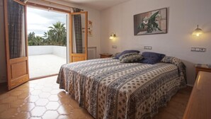 Un dormitorio con cama, un cuadro y vistas al balcón por una puerta abierta.