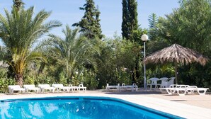Una piscina con sillones de descanso y un paraguas de paja.