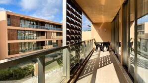 Ein moderner Balkon mit Glasgeländern, einer Sitzecke und Blick auf benachbarte Gebäude.