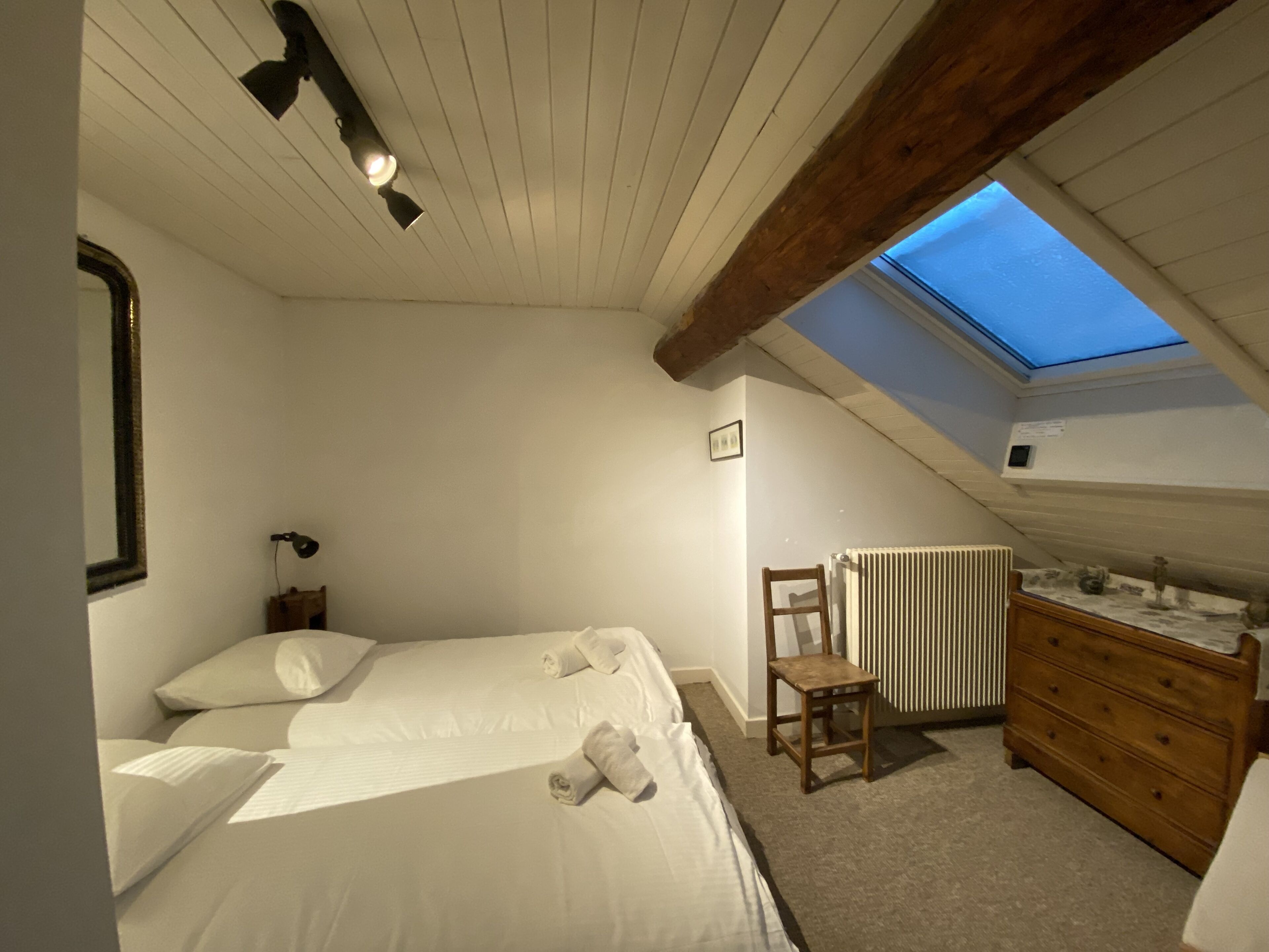 A bedroom with a skylight, a bed, a chair, a dresser, and a radiator.