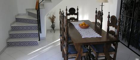 Un espace repas comprenant une table en bois, des chaises et un escalier dont les marches sont décorées de motifs.
