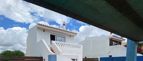 Un patio cubierto con piscina, un pequeño jardín con estatua de rana y un edificio blanco con puerta azul.