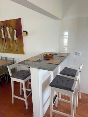 Une cuisine dotée d’un plan de travail en granit, de chaises blanches, d’un tableau et d’un pare-feu en carreaux.