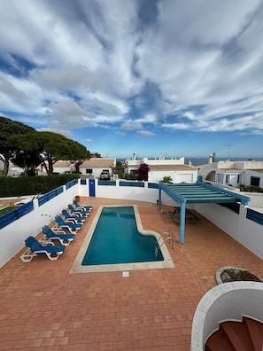 Une piscine sur le toit, avec des chaises longues bleues, une pergola et une vue sur la mer.
