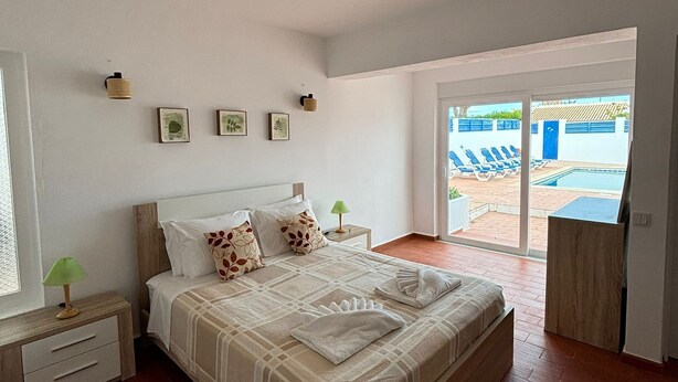 A bedroom with a bed, a nightstand, a window, and a view of an outdoor swimming pool. - 2-bed Villa with Private Pool and Panoramic Views in a quiet residential area (Lagos)