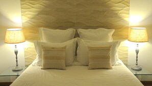 A bed with white bedding, two bedside lamps, and a textured wall behind.