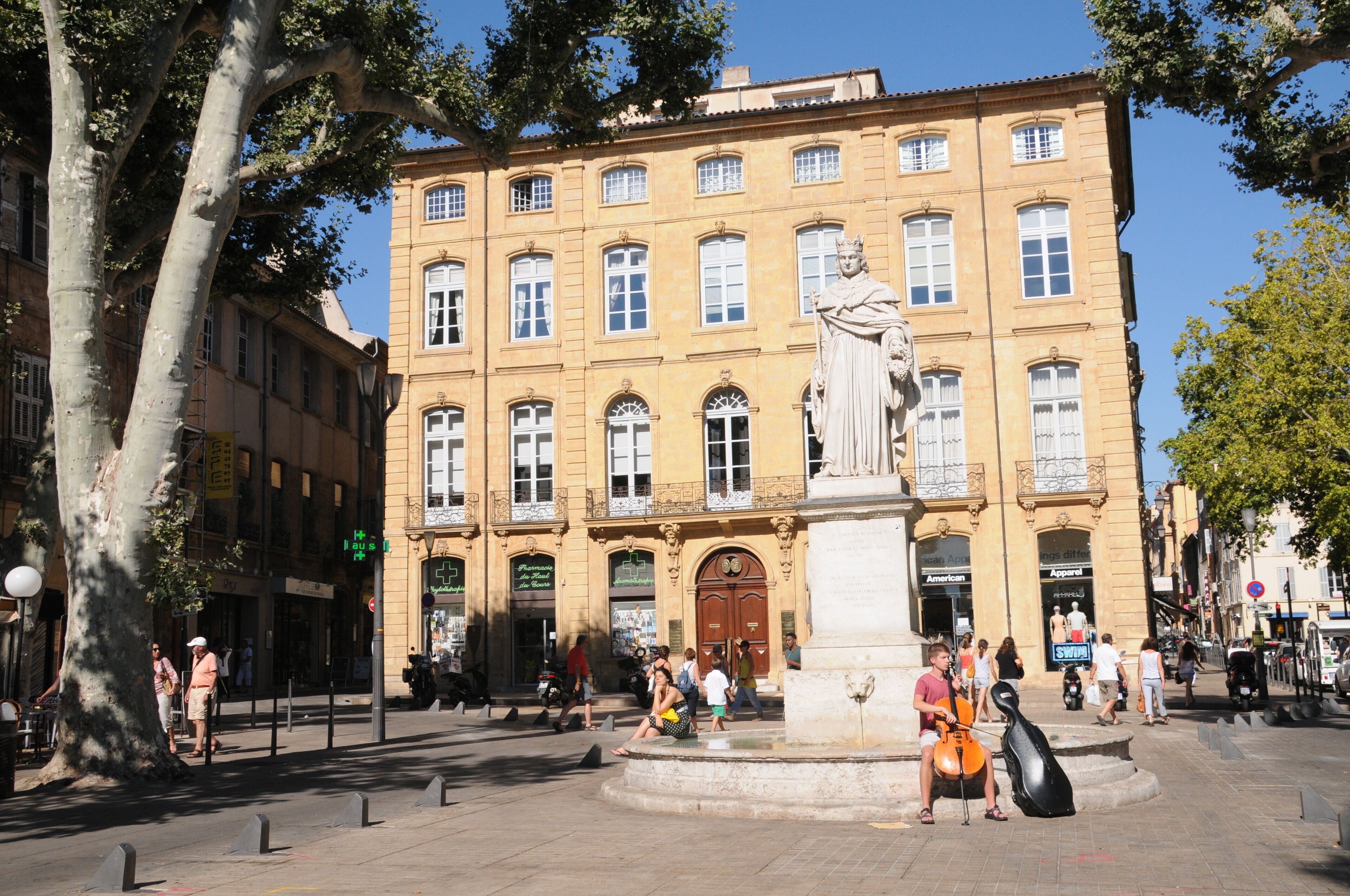 A public square with a statue, a fountain, and a building with multiple windows and balconies.