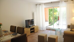 A living room with a TV on a wooden stand, a dining table set with plates and glasses, and a sofa.