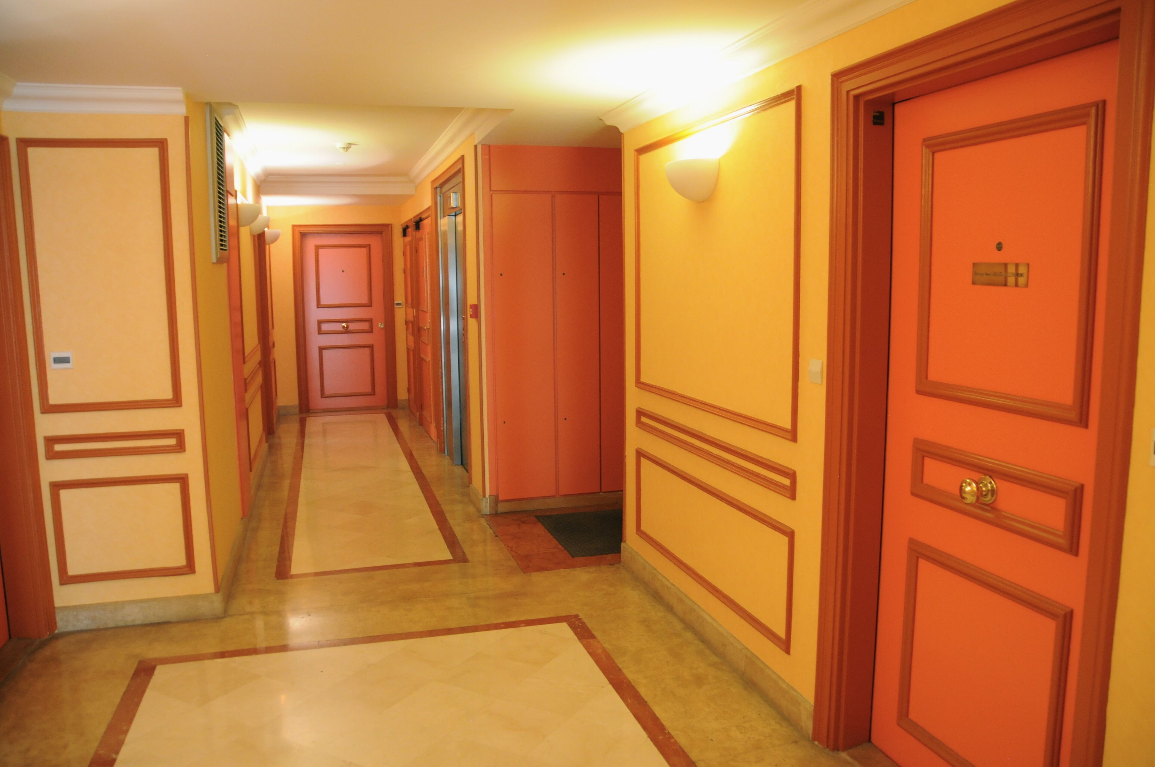A hotel corridor with multiple doors, a tiled floor, and a light fixture on the wall.