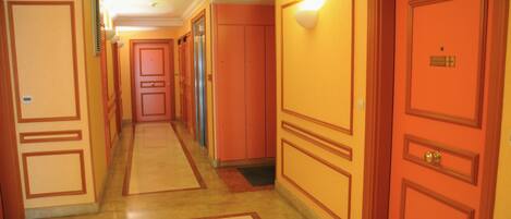 A hotel corridor with multiple doors, a tiled floor, and a light fixture on the wall.