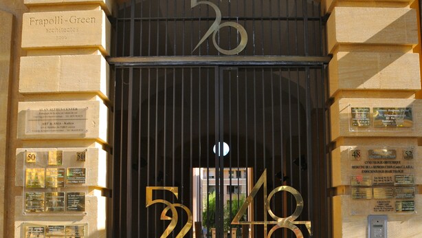 A building entrance with a large arched doorway, a number plaque, and several informational plaques on the walls.