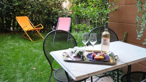 An outdoor dining area with a table set for two, featuring a bottle of wine, glasses, and a plate of macarons.