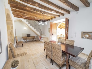 Una zona de menjador amb taula de fusta i cadires de vimetla, una escala i un disseny interior rústic.