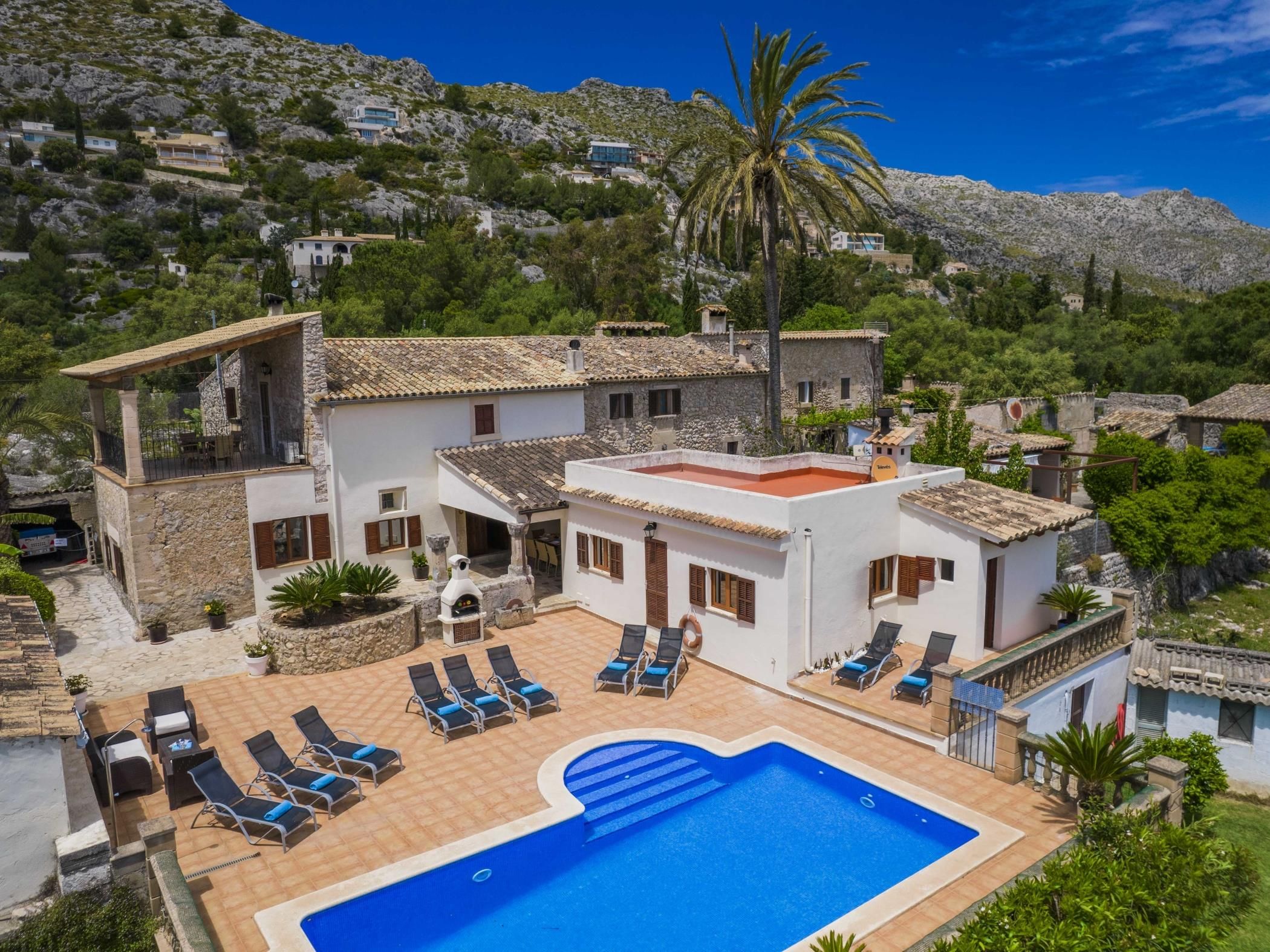 A villa with a swimming pool, sun loungers, and a view of the surrounding hills.