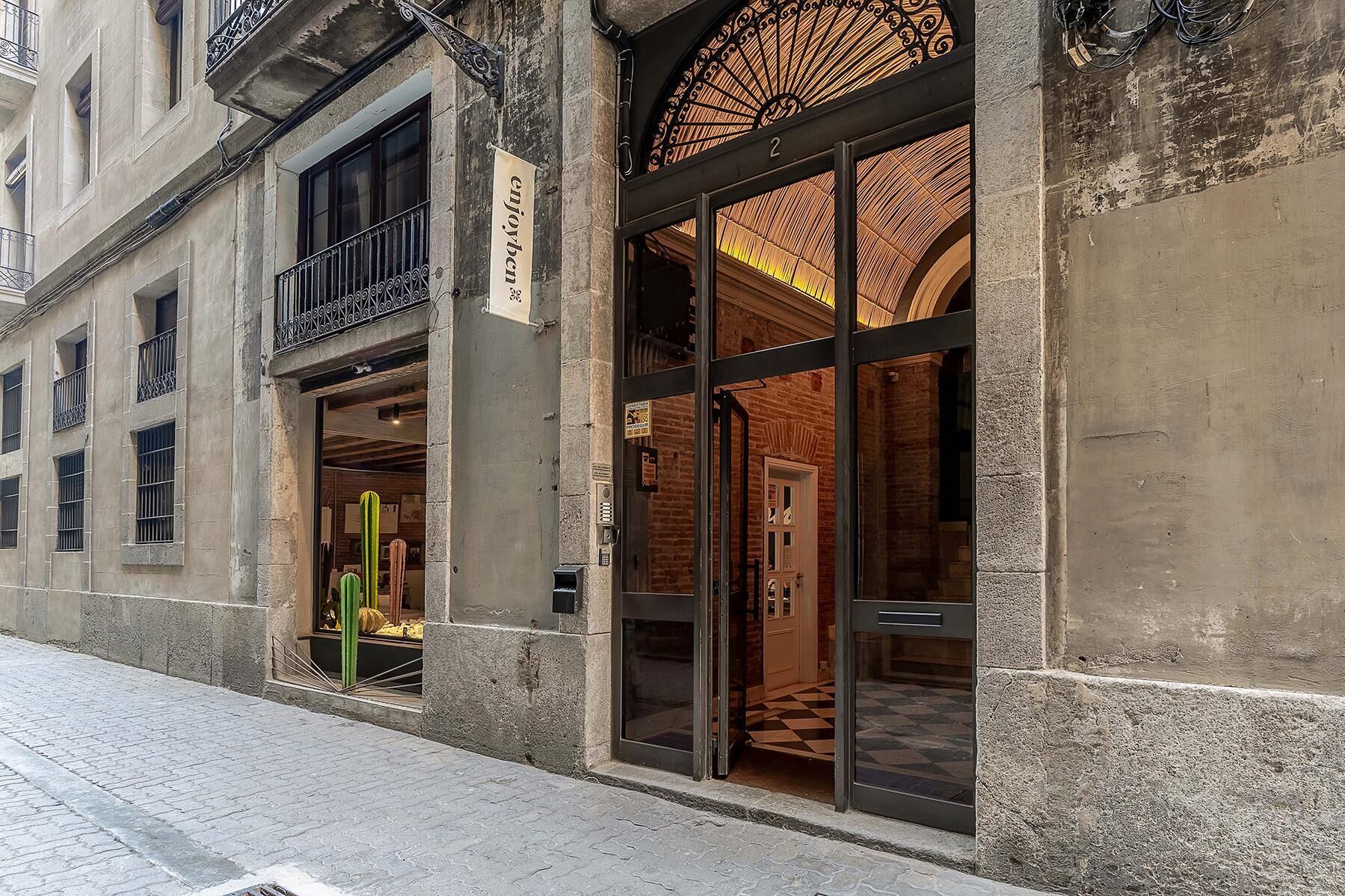Un edificio con una amplia entrada de vidrio, un letrero que dice "enjoyben" y una puerta visible en el interior.