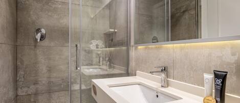 A modern bathroom with a glass-enclosed shower, a white sink, and a large mirror.