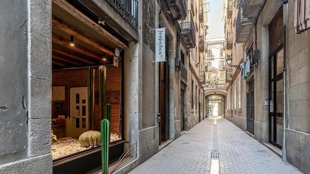 A narrow cobblestone alley with a storefront on the left and a building on the right. - Apartment with maritime essence in an unbeatable location (Barcelona)
